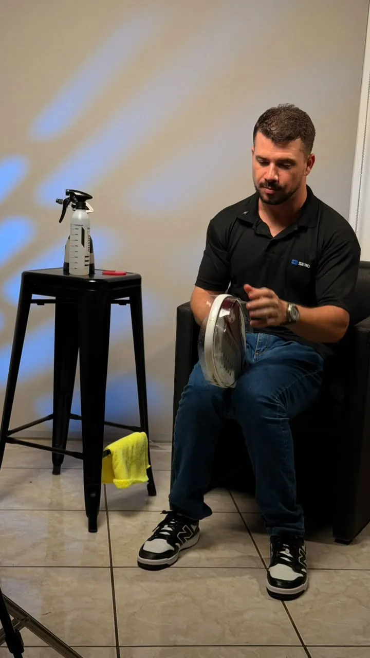 Ronan aplicando película de proteção numa raquete branca, com borrifador e pano de microfibra ao lado